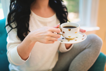 Young woman holding a cup of coffee in a chair in her homeの写真素材