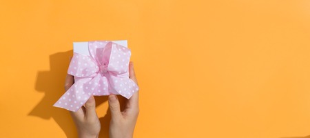 Woman holding a gift box on a orange background