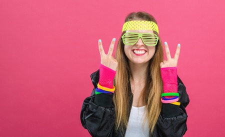 Woman in 1980s fashion giving the peace sign on a pink background