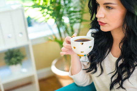 Young woman drinking coffee in a chair in her homeの写真素材
