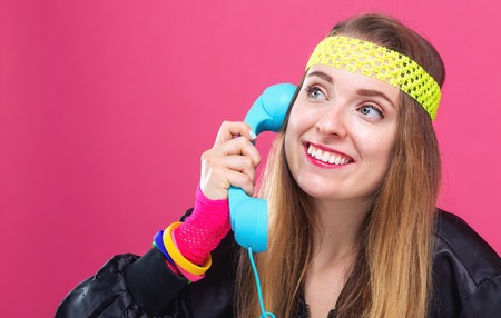 Woman in 1980s fashion with old fashioned phone on a pink background