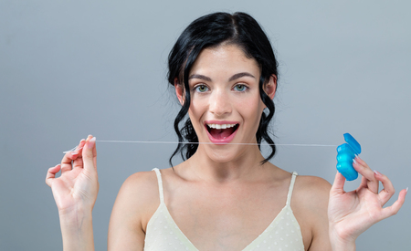 Young woman with dental floss on a gray background