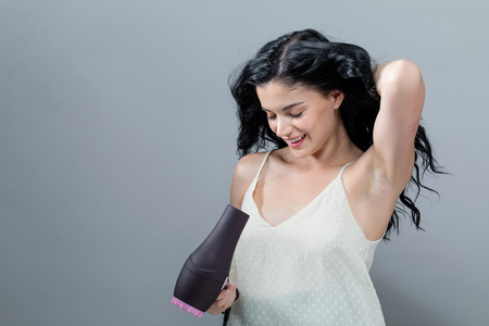 Beautiful young woman holding a hairdryer on a gray backgroundの写真素材