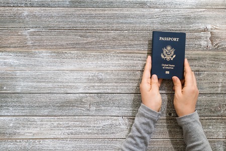 Person holding a US passport on a wooden desk from above