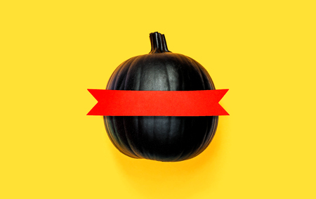 Black pumpkin with red banner on a yellow backgroundの写真素材