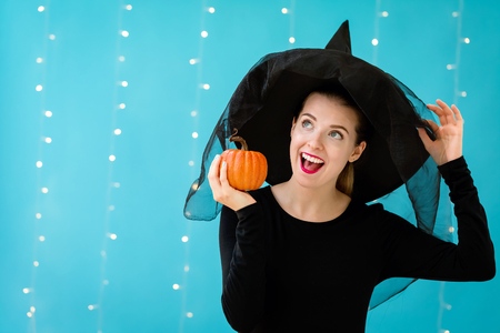 Young woman with a witch hat holding a halloween pumpkin on a shiny light backgroundの写真素材