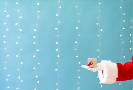 Santa holding a small Christmas gift on a shiny light blue background