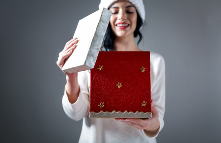 Young woman opening a Christmas present box on a gray backgroundの写真素材