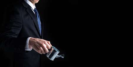 Businessman with watering can concept on a black backgroundの写真素材