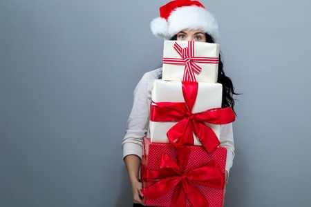 Young woman with santa hat holding gift boxes on a gray backgroundの写真素材