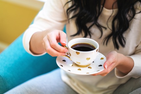 Young woman holding a cup of coffee in a chair in her homeの写真素材