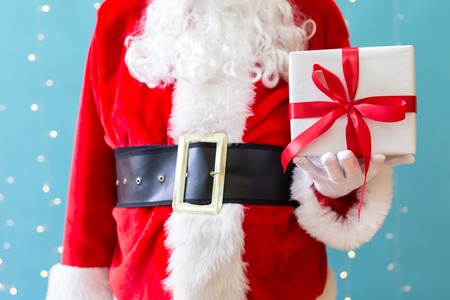Santa holding a Christmas gift on a shiny light blue backgroundの写真素材