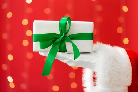 Santa holding a Christmas gift on a shiny light red background