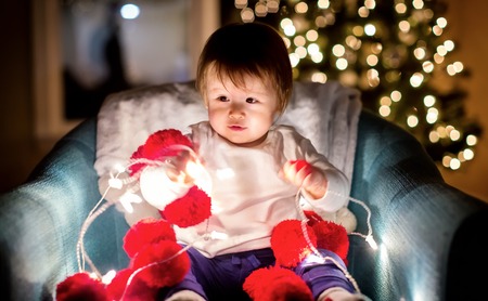 Toddler boy playing with Christmas lights in his house at Christmas time