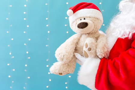 Santa holding a teddy bear on a shiny light blue backgroundの写真素材