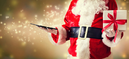 Santa holding a tablet computer on a shiny light backgroundの写真素材