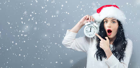 Young woman holding a clock showing nearly 12 on a gray backgroundの写真素材