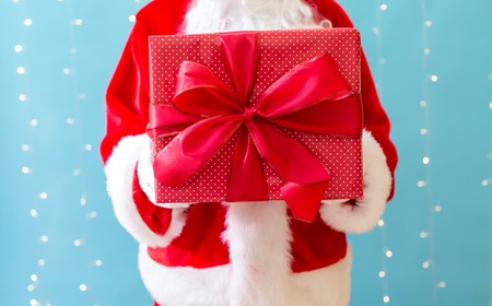 Santa holding a Christmas gift on a shiny light blue backgroundの写真素材