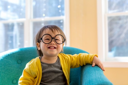 Happy toddler boy with glasses playing in a big chair