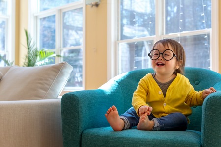 Happy toddler boy with glasses playing in a big chairの写真素材