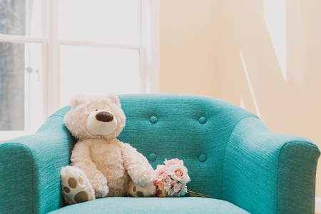 Teddy bear and a flower bouquet on a chair in a roomの写真素材