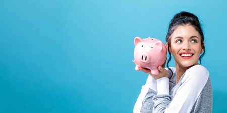 Young woman with a piggy bank on a solid backgroundの写真素材