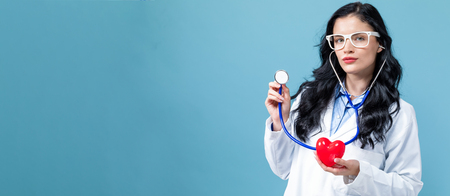 Medical doctor with a stethoscope and a heart health concept on a blue backgroundの写真素材
