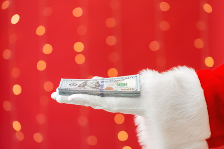 Santa holding US dollar bills on a shiny light red backgroundの写真素材