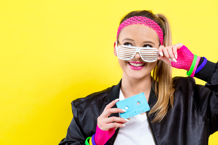 Woman in 1980s fashion holding a cassette tape on a split yellow background