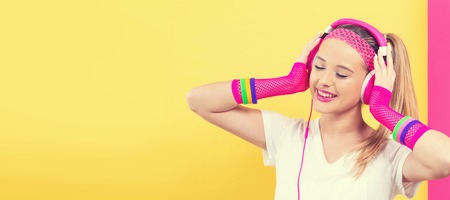 Woman in 1980s fashion with headphones on a split yellow and pink backgroundの写真素材