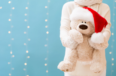 Woman holding a teddy bear with Santa hat on a shiny light blue backgroundの写真素材