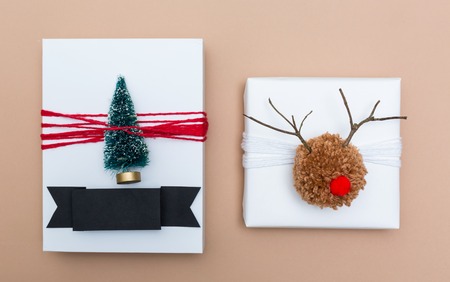 Pompom reindeer and miniature Christmas tree gift boxes on a light brown paper backgroundの写真素材