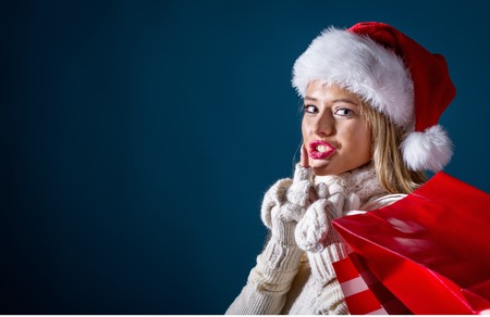 Young woman with santa hat holding shopping bags on a dark blue backgroundの写真素材
