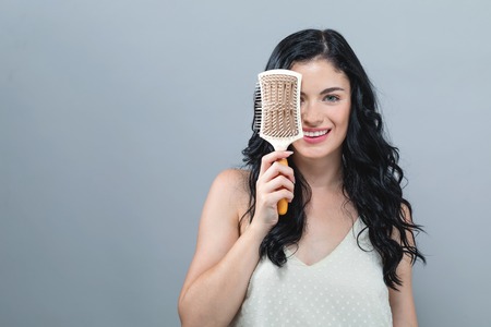 Beautiful young woman holding a hairbrush on a gray background