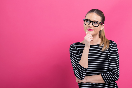 Young woman in a thoughtful pose on a pink backgroundの写真素材