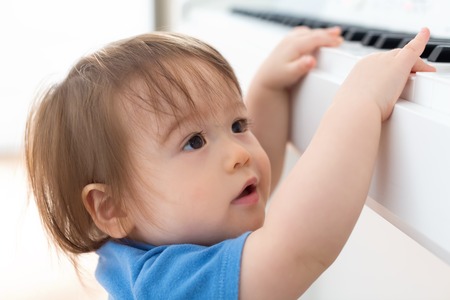 Toddler boy excited to reach up and play the pianoの写真素材