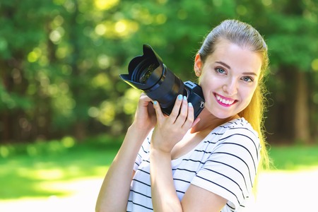 Young woman with a professional digital SLR camera on a bright summer day in the forest