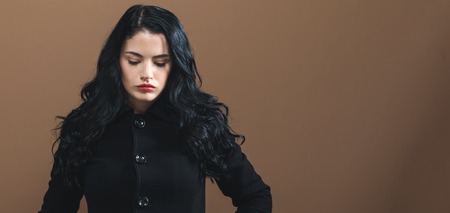 Beautiful young woman in a fashionable coat on a brown backgroundの写真素材