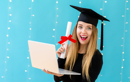 Young woman with a graduation diploma and laptop pc on a shiny light backgroundの写真素材