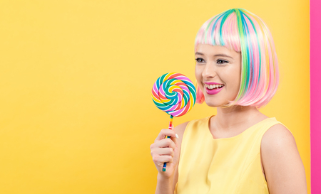 Woman in a colorful wig with a giant lollipop on a split yellow and pink backgroundの写真素材
