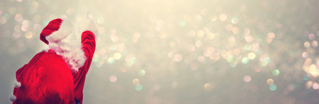 Santa pointing at the sky on a shiny light backgroundの写真素材