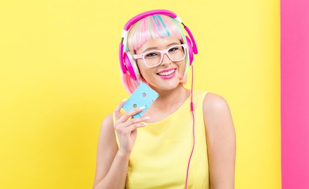 Woman with cassette tape and bright colorful wig on a split yellow and pink backgroundの写真素材
