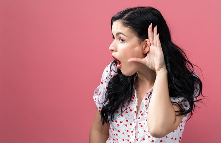 Young woman listening on a pink background