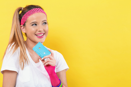 Woman in 1980s fashion holding a cassette tape on a yellow background