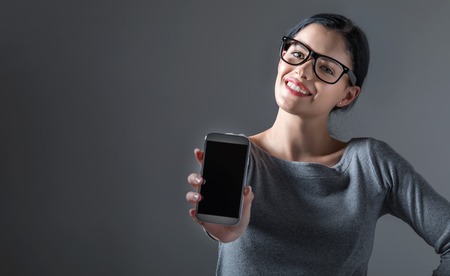 Young woman holding out a cellphone in her hand on a gray backgroundの写真素材