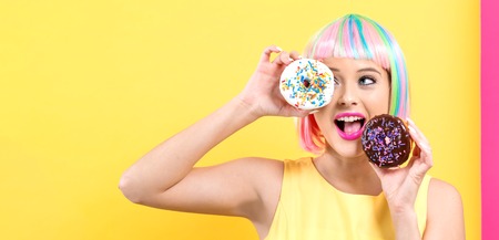 Beautiful woman in a colorful wig with doughnuts on a split yellow and pink backgroundの写真素材