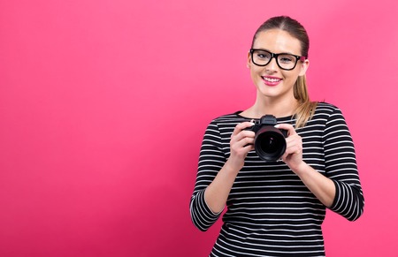 Young woman with a professional digital SLR camera on a pink backgroundの写真素材