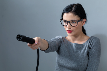 Young woman with an electric vehicle charger on a gray backgroundの写真素材