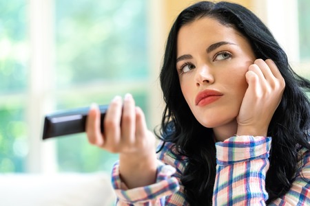 Young woman holding a TV remote control in her homeの写真素材
