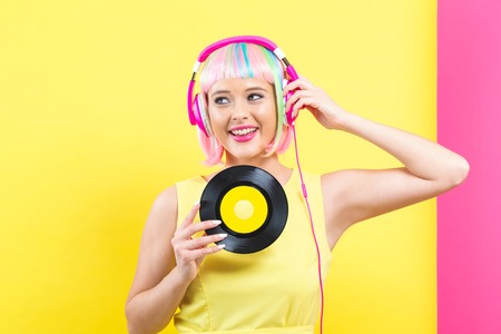 Woman in a colorful wig holding a vinyl record on a split yellow and pink backgroundの写真素材